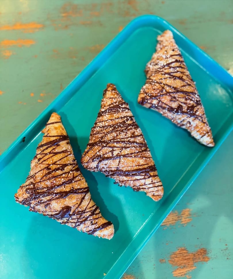 Three triangular pastries with chocolate drizzle and powdered sugar on a teal tray.